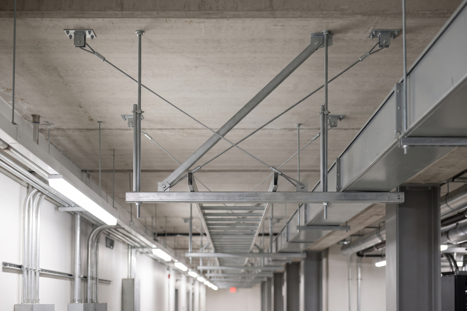 Cable tray and busway on threaded-rod trapeze hangers with diagonal seismic cable and strut braces to the concrete slab above.