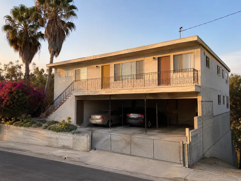 Two-story stucco apartment building in North Hollywood with open tuck-under carport on a hillside lot.