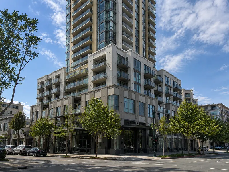 High-rise condominium tower in Oakland, CA, with multi-level podium balconies and glass guardrails — subject to SB-326 inspection.