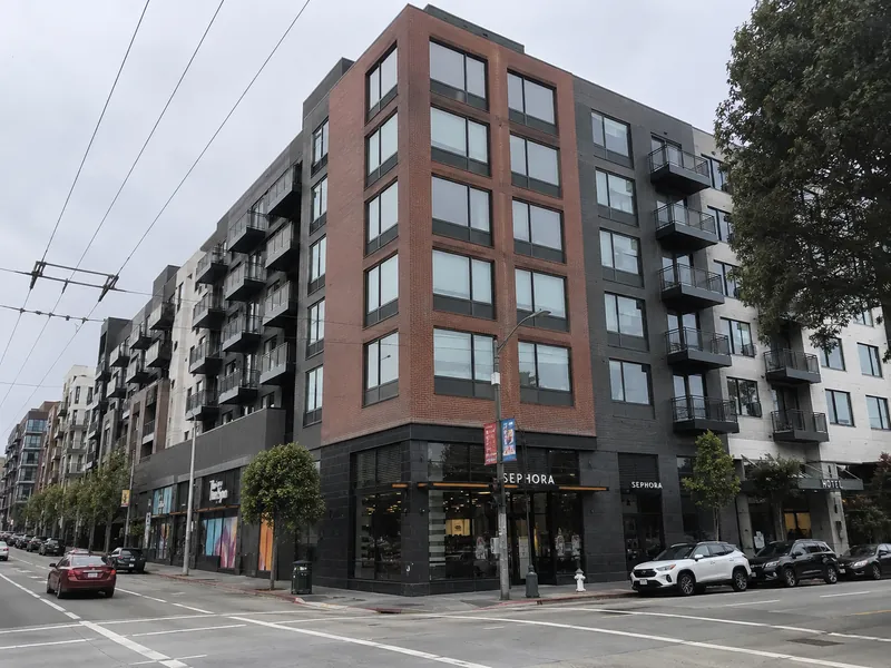 Six-story mixed-use multifamily building with ground-floor retail and projecting steel-rail balconies at a San Francisco street corner.